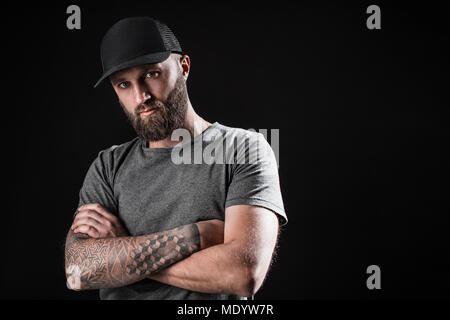 Homme barbu noir pensive vêtu d'une chemise grise, lunettes de soleil et casquette de baseball. Banque D'Images