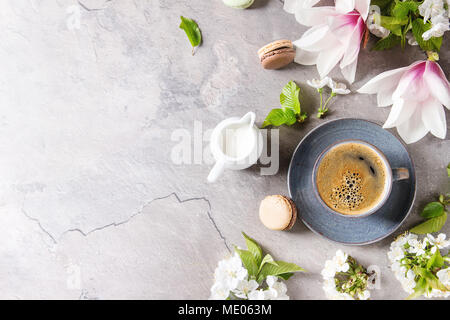 Blue tasse de café espresso noir, dessert français macarons, crème et fleurs de printemps magnolia, blooming cherry branches sur fond texture gris. Banque D'Images