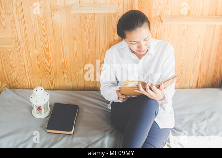 Soft image de jeune femme Asain lecture livre sur son lit dans la chambre Banque D'Images