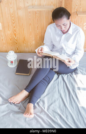 Soft image de jeune femme Asain lecture livre sur son lit dans la chambre Banque D'Images