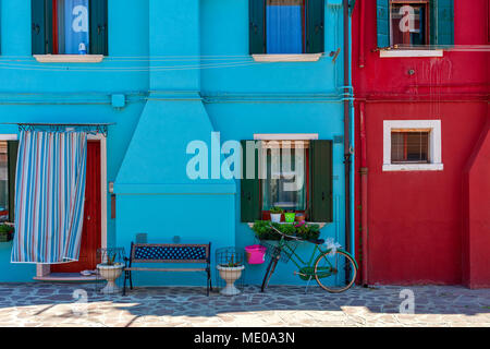 Petit banc et location en face de petites maisons peintes de couleurs bleu et rouge à Burano, Italie. Banque D'Images