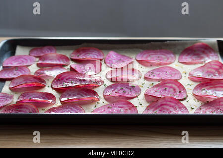 Tranches de betterave chioggia betterave (bonbons) sur une plaque à pâtisserie doublée, prêt pour faire des copeaux de légumes au four. Banque D'Images