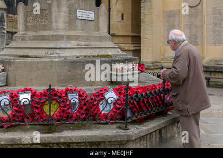 Homme âgé met une petite croix sur Cirencester War Memorial est ensuite et se rappelle le passé en regardant les coquelicots et couronnes Banque D'Images