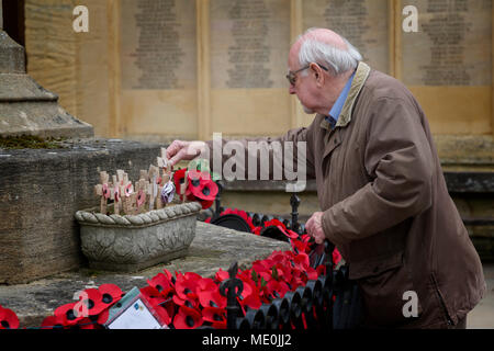 Homme âgé met une petite croix sur Cirencester War Memorial est ensuite et se rappelle le passé en regardant les coquelicots et couronnes Banque D'Images