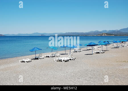 Plage avec parasols bleus sur la côte méditerranéenne à Fethiye, Turquie. Banque D'Images