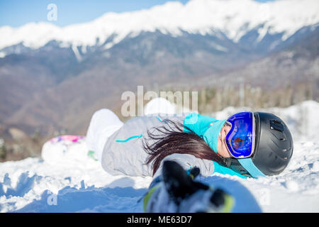 Photo de jeune femme au casque et avec snowboard couché sur la pente de montagne Banque D'Images