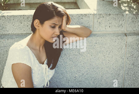 Closeup portrait, sourde colère triste jeune femme en robe blanche assise sur banc, déprimé, bas, isolé sur fond gris. Émotion négative feeli Banque D'Images