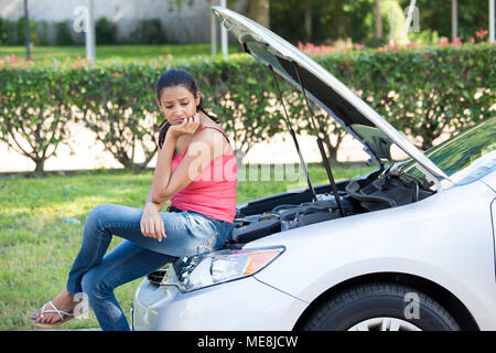 Closeup portrait, jeune femme en rose tanktop des ennuis avec sa voiture cassée, assis sur le capot ouvert, inquiets du moteur vert des arbres et des arbustes isolés Banque D'Images