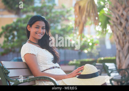 Closeup portrait young Beautiful woman in white dress, assis sur un banc isolé, palmiers, vert nature background. L'émotion positive fa Banque D'Images