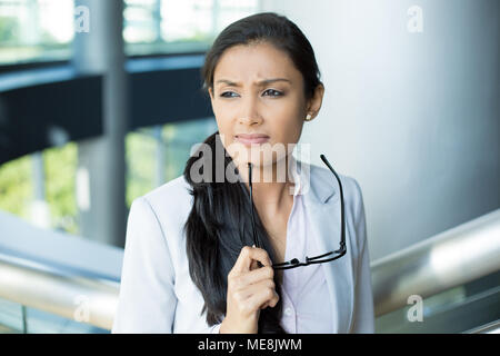 Closeup portrait, femme leader en costume gris avec des lunettes noires sous le menton en réfléchissant, cogitative, nécessitant de prendre des décisions difficiles, isolées à l'intérieur Banque D'Images