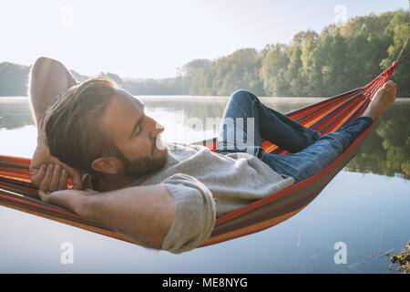 Jeune homme sur hamac détente au bord de la lac dans le matin, la lumière du soleil. Les gens voyagent bien-être la paresse concept. France, Europe Banque D'Images
