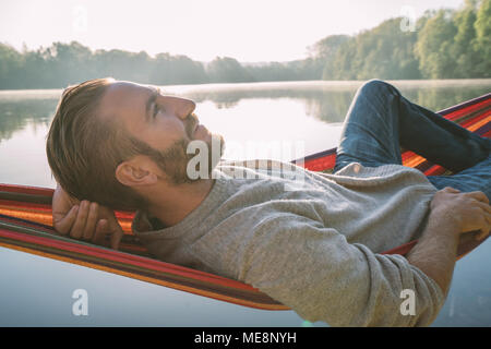 Jeune homme sur hamac détente au bord de la lac dans le matin, la lumière du soleil. Les gens voyagent bien-être la paresse concept. France, Europe Banque D'Images