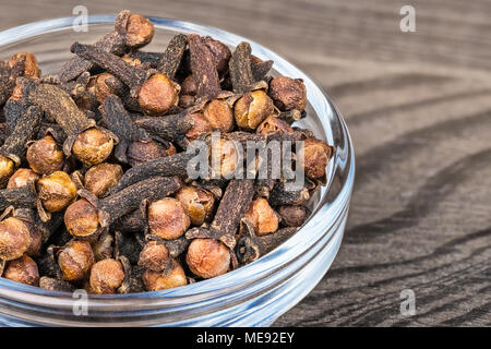 Close-up de séché épicé de girofle. Syzygium aromaticum. Bol en verre décoratif plein d'épices médicinales aromatiques avec parfum distinctif sur fond de bois. Banque D'Images