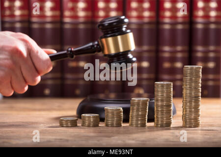 Close-up d'un juge's Hand Holding Gavel Plus de pièces d'or empilés Banque D'Images