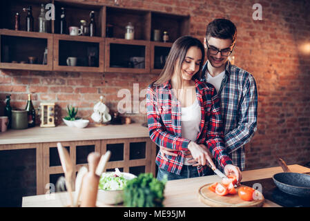 Mari hugs femme pendant qu'elle la cuisson dans un bol à salade de légumes frais sur la cuisine. Le régime alimentaire la préparation des aliments. Couple prépare un dîner romantique, vie saine Banque D'Images