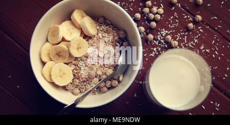 Petit déjeuner sain. Bol de céréales à la banane, les raisins secs et les noix. Et un verre de lait sur le fond de bois. Vue d'en haut. La photo en gros plan. Sweet vegan dis Banque D'Images