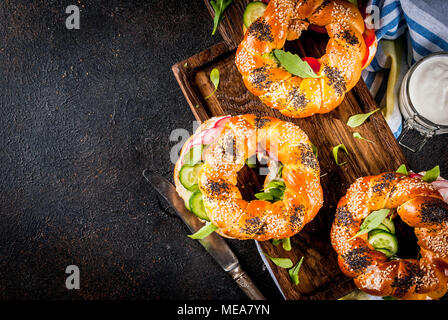 Variété de sandwiches bagels faits maison avec le sésame et les graines de pavot, fromage à la crème, jambon, radis, roquette, tomates, concombres, sur une planche à découper. Banque D'Images