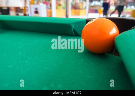 Une piscine orange ball accroche précairement sur une poche n'une table de billard. Banque D'Images