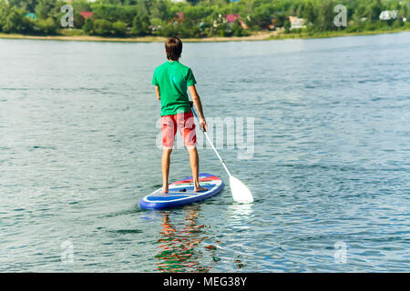 Homme surf sup stand up paddle boarder pagayer au coucher du soleil sur la rivière. Banque D'Images