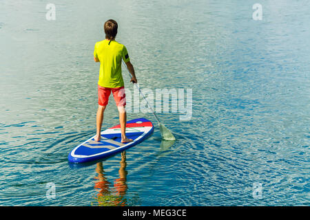 Homme surf sup stand up paddle boarder pagayer au coucher du soleil sur la rivière. Banque D'Images