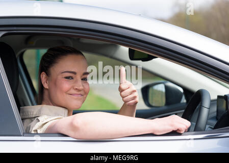 Belle jeune femme au volant de sa toute nouvelle voiture et en montrant son pouce vers le haut Banque D'Images