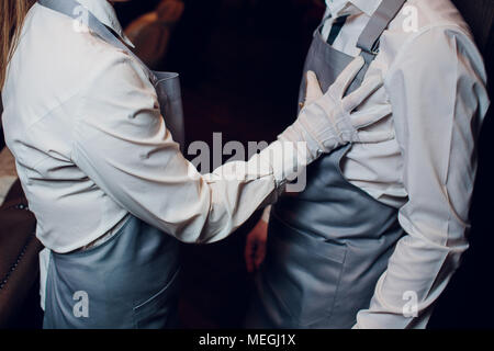 Jeunes chefs ou maîtres d'homme et de la femme pose, méconnaissable fille garçon touche la poitrine méconnaissable waiter en gants blancs tablier gris restau Banque D'Images