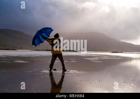 Ardara, comté de Donegal, Irlande la météo. 22 avril 2018. Un homme aux prises avec un parapluie tout en prenant une promenade sur la plage par un jour de vent avec beaucoup d'averses de pluie sur la côte ouest. Crédit : Richard Wayman/Alamy Live News Banque D'Images