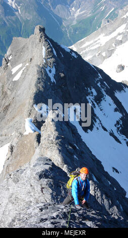 Homme d'alpiniste sur son chemin à un haut sommet alpin sur une pente raide et exposé sur la crête de roche d'une belle journée d'été Banque D'Images