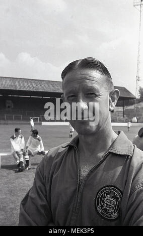 1964, tableau historique, à l'entraîneur de Charlton Athletic FC à leur terrain de football, la vallée, avec des joueurs derrière lui sur le terrain. Sa partie supérieure comporte une grande d'un insigne indiquant qu'il est un entraîneur de l'English Football Association (FA) Banque D'Images