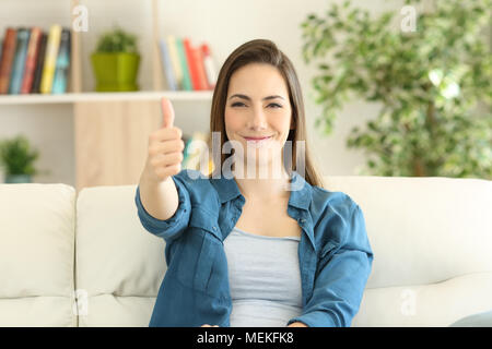 Satisfait woman looking at camera with Thumbs up assis sur un canapé dans la salle de séjour à la maison Banque D'Images