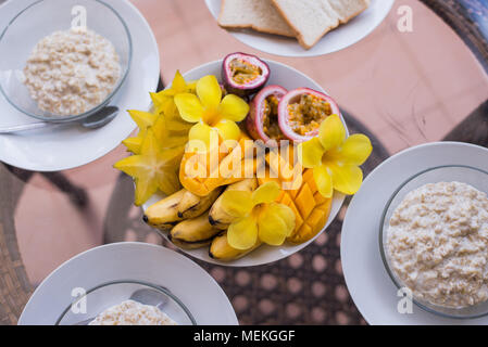 Délicieux petit-déjeuner maison servi pour trois personnes. Oatmeals porrige et corbeille de fruits à la mangue, banane, fruit de la passion et de fleurs. Service moderne Banque D'Images