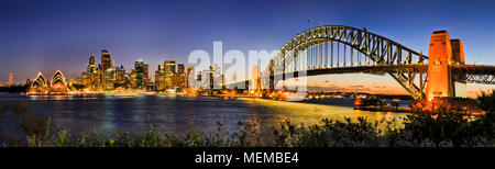 De soleil colorés sur la ville de Sydney CBD landmarks autour de Sydney Harbour à Sydney Harbour Bridge arch illuminé se reflétant dans les eaux brouillées. Banque D'Images