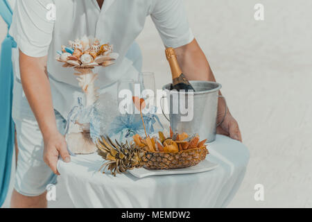 Décoration de table avec bouteille de champagne, refroidisseur, verres et fruits. Les préparatifs de mariage à la plage tropicale. Banque D'Images