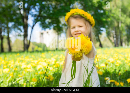 Petite fille avec une couronne de fleurs sur la tête, ce qui vous bouquet de pissenlits Banque D'Images