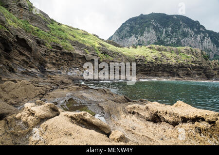La formation de lave de falaises avec partie supérieure verte avec vue sur le mont Sanbangsan à Yongmeori Beach, Sanbang-ro, l'île de Jeju, Corée du Sud Banque D'Images
