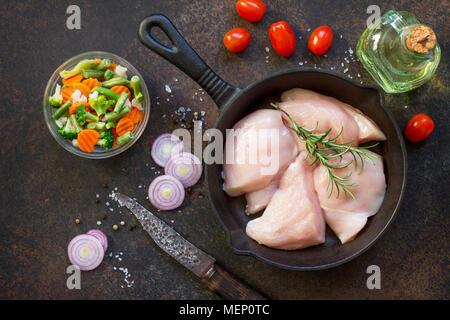 La viande fraîche. Filet de poulet crus sur un poêle en fonte, d'épices et de légumes frais sur une table de cuisine. Banque D'Images