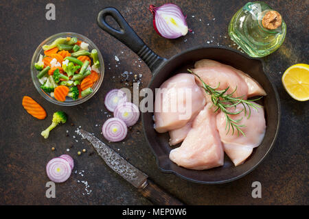 La viande fraîche. Filet de poulet crus sur un poêle en fonte, d'épices et de légumes frais sur une table de cuisine. Banque D'Images