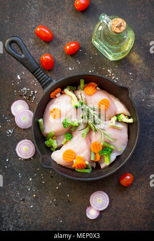La viande fraîche. Filet de poulet crus sur un poêle en fonte, d'épices et de légumes frais sur une table de cuisine. Banque D'Images