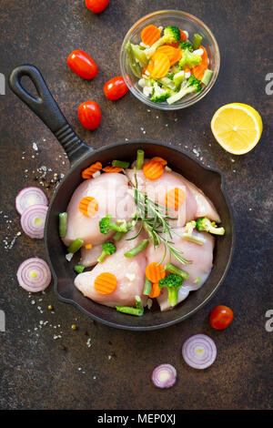 La viande fraîche. Filet de poulet crus sur un poêle en fonte, d'épices et de légumes frais sur une table de cuisine. Banque D'Images