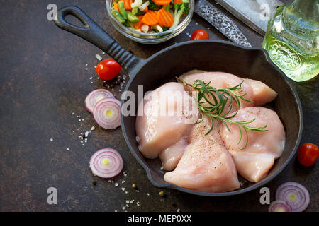 La viande fraîche. Filet de poulet crus sur un poêle en fonte, d'épices et de légumes frais sur une table de cuisine. Banque D'Images