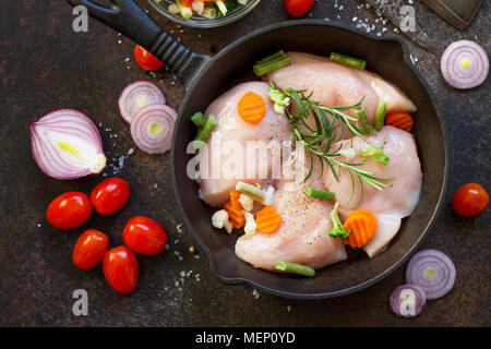 La viande fraîche. Filet de poulet crus sur un poêle en fonte, d'épices et de légumes frais sur une table de cuisine. Banque D'Images
