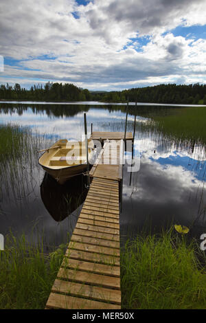 Un bateau à rames est amarré à une jetée dans un lac forêt vitreux Banque D'Images