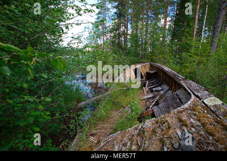 Un vieux bateau en bois en décomposition est au bord d'un lac de forêt. Banque D'Images