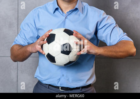 Businessman in a blue shirt se tient près du mur et est titulaire d'un ballon de football dans ses mains. Banque D'Images