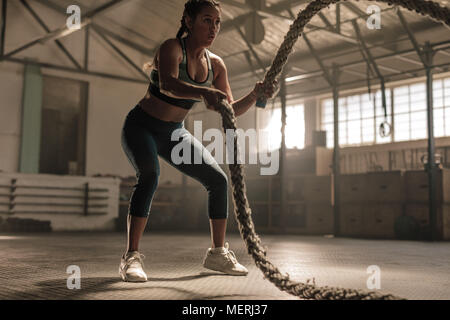 Jeune femme faisant la formation de force à l'aide de cordes de bataille dans la salle de sport. Déménagement de l'athlète les cordes en mouvement de vague dans le cadre de la combustion des graisses entraînement. Banque D'Images