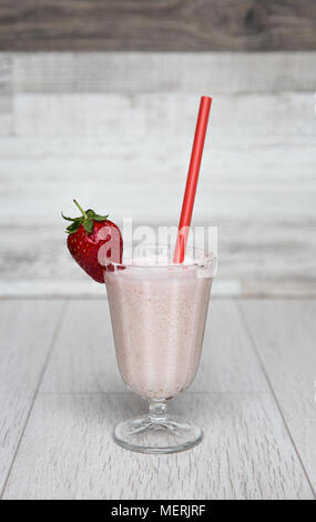 Un rose pastel strawberry milkshake smoothie ou dans un grand verre et décoré avec des fruits et une paille rouge sur un fond blanc. Banque D'Images