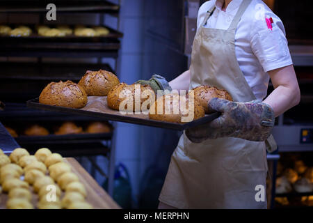 Un mâle Baker en uniforme blanc et un tablier beige prend le pain d'un four industriel. Travailler à la boulangerie Banque D'Images