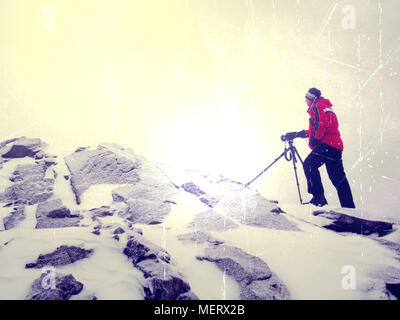 Effet abstrait. Photographe de voyage faisant photos dans les pierres sur le pic enneigé de montagne. Hiver froid et brumeux matin dans les montagnes Banque D'Images