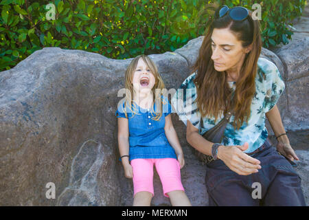 Quatre ans fille blonde avec robe denim bleu, assis sur le banc en pierre avec la mère, à la femme en colère et de crier Banque D'Images