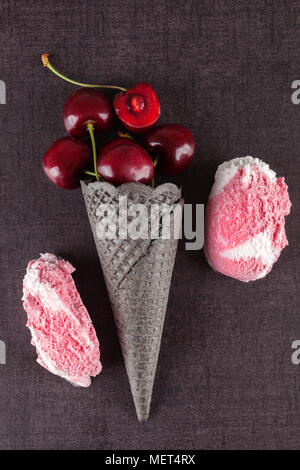 De délicieuses glaces en cornet gaufré noir avec cerises fraîches sur la surface noire du dessus. Banque D'Images